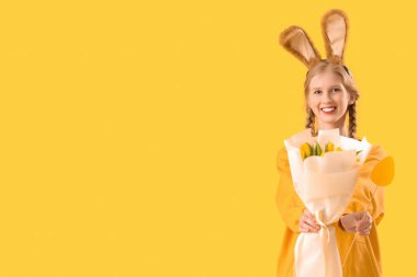 Paskalya tavşanı kulakları, çiçekleri ve sarı arka planda kağıt yumurtası olan genç bir kız.