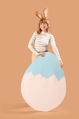 Paskalya tavşanı kulaklı genç bir kız ve bej arka planda büyük bir kağıt yumurta.