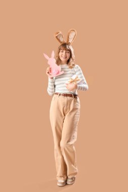 Paskalya tavşanı kulaklı genç kız, kağıttan tavşan ve bej arka planda hediye.