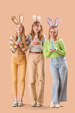 Paskalya tavşanı kulaklı genç kızlar ve bej arka planda oyuncak tavşanlar.