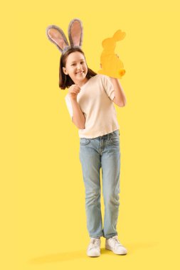 Paskalya tavşanı kulakları ve sarı arka planda dekoratif tavşanı olan sevimli küçük bir kız.