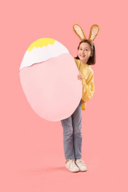 Paskalya tavşanı kulakları ve pembe arka planda büyük kağıt yumurtası olan tatlı küçük bir kız.