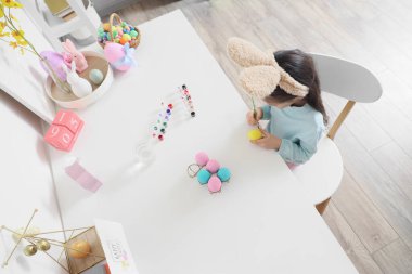 Tavşan kulağı takan tatlı küçük kız evde paskalya yumurtası boyuyor.