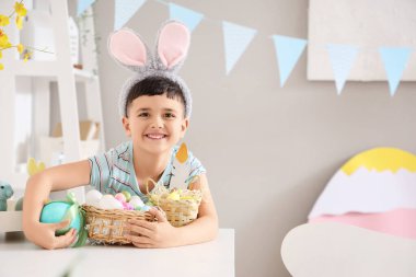 Evde paskalya hediyesi yumurta ve sepetle tavşan kulağı takan şirin bir çocuk.