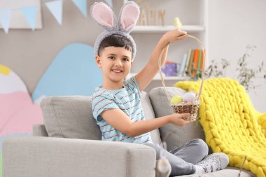 Evde paskalya sepetiyle tavşan kulağı takan şirin bir çocuk.
