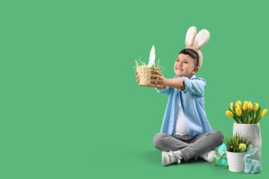 Paskalya sepeti, laleler ve yeşil arka planda tavşan takan sevimli küçük bir çocuk.