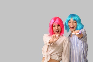 Gri arka planda parti düdüğü çalan peruklu güzel, genç ve mutlu kadınlar. 1 Nisan şakası