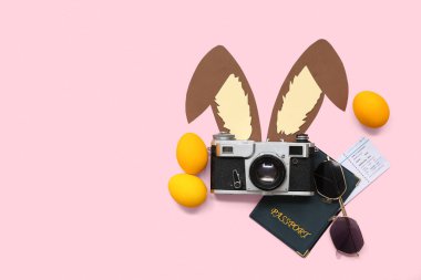 Pasaport, güneş gözlüğü ve pembe arka planda Paskalya dekoru olan bir kamera. Tatil seyahati kompozisyonu