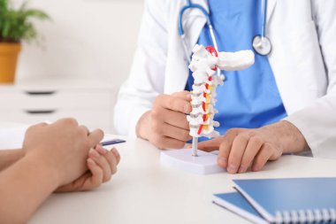 Omurga modelini klinikteki hastaya açıklayan erkek doktor, yakın plan.