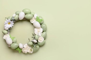 Beyaz çiçekli Paskalya çelengi, açık yeşil arka planda yumurta ve kelebekler.