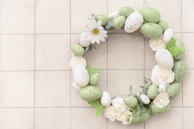 Beyaz fayans üzerinde çiçekler, yumurtalar ve kelebeklerden oluşan Paskalya çelengi.