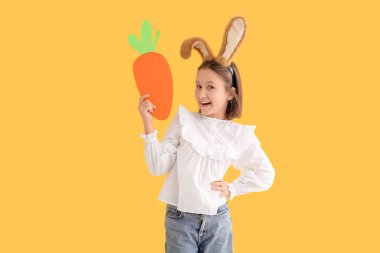 Paskalya tavşanı kulaklı mutlu küçük kız sarı arka planda kağıt havuç