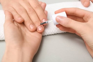Manikür ustası gri arka planda erkek tırnaklarına tırnak altı yağı sürüyor.