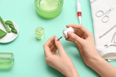Tırnaklara, aloe veraya ve turkuaz arka planda manikür aletlerine tırnak yağı süren kadın eller