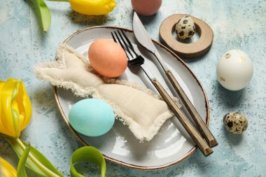 Paskalya yumurtaları, oyuncak tavşancık ve açık mavi arka planda sarı lalelerle güzel bir masa.