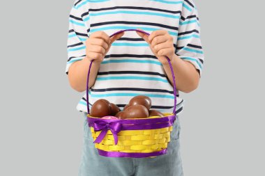 Beyaz arka planda Paskalya için çikolatalı yumurta sepeti tutan küçük çocuk.