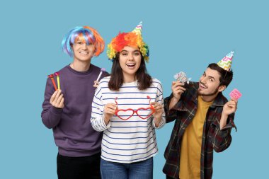 Mavi arka planda düdük ve kağıt etiketli komik kılık değiştirmiş genç arkadaşlar. 1 Nisan kutlamaları