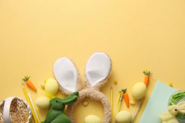 Tavşan kulaklı, Paskalya yumurtası ve sarı arka planda okul malzemeleri.