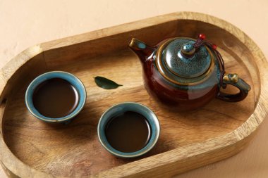 Seramik çaydanlıklı ahşap tepsi ve bej arka planda sıcak demlenmiş çay.