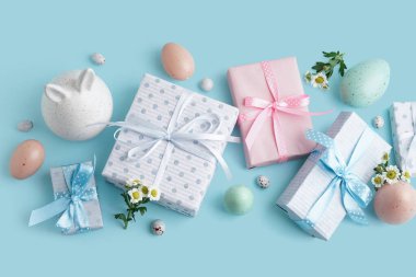 Hediye kutularıyla boyanmış Paskalya yumurtaları, papatya çiçekleri ve mavi arka planda bir tavşan.