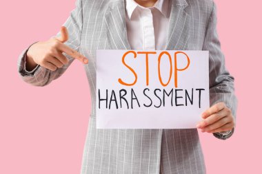 Genç iş kadını, pembe arka planda DUR HARASSMENT ile kağıda işaret ederek, yakın plan