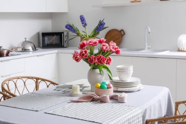 Mutfaktaki yemek masasında vazo lale, paskalya yumurtası ve yemek takımı.