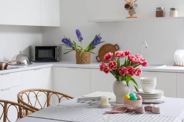 Mutfaktaki yemek masasında vazo lale, paskalya yumurtası ve yemek takımı.