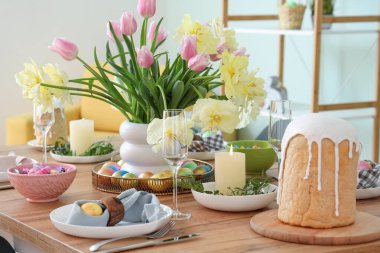 Şenlikli masa dekorları, boyanmış yumurtalar, Paskalya pastası ve çiçek vazosu.