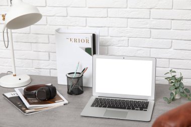 Modern dizüstü bilgisayarı, lambası ve beyaz tuğla duvarın yanında kırtasiyesi olan şık bir iş yeri.