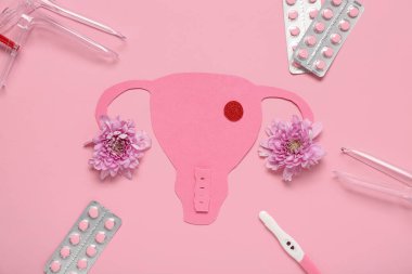 Pembe arka planda jinekolojik spekulumlu kağıt rahim, haplar ve hamilelik testi.