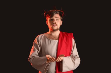 İsa cüppeli bir adam ve siyah arka planda kırmızı ışığı olan dikenli bir taç.