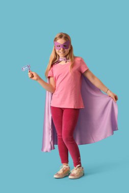 Mavi arka planda otlakçı ve karnaval maskesi olan süper kahraman kostümlü şirin küçük bir kız. Purim kutlaması