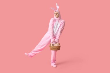 Paskalya tavşanı kostümlü mutlu genç adam pembe arka planda sepet tutuyor.