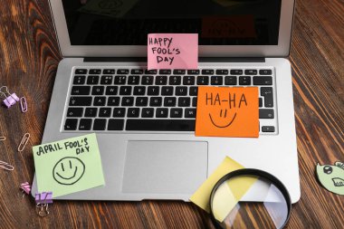 Diz üstü bilgisayar ve tahta arka planda yapışkan notlar. 1 Nisan şakası.