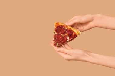 Kadın elleri bej arka planda lezzetli pizza dilimleri tutuyor.