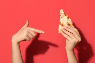 Kırmızı arka plandaki lezzetli pizza dilimini gösteren kadın elleri.