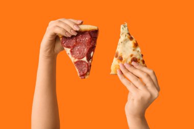 Turuncu arka planda lezzetli pizza dilimleri tutan kadın eller.