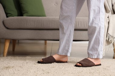 Evdeki kanepenin yanındaki yumuşak terlikli adam.