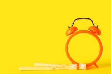 Sarı arka planda çalar saat ve diş fırçaları