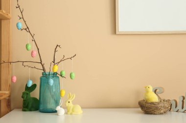 Mavi cam vazoda Paskalya yumurtaları ve bej arka planda Paskalya tavşanları.