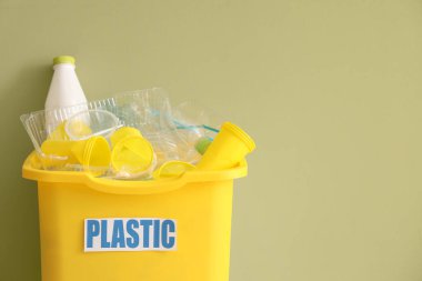 Yeşil duvarın yanında plastiği olan sarı geri dönüşüm kutusu. Geri dönüşüm kavramı