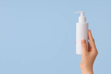 Mavi arka planda el kremi şişesi olan kadın.