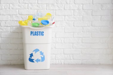 Beyaz tuğla duvarın yanında PLASTIC işareti olan tam çöp kutusu. Geri dönüşüm kavramı