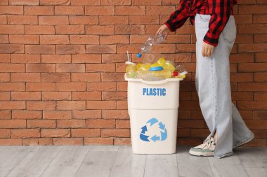 Kadın, plastik levhası tuğla duvarın yanında olan bir çöp kutusuna koyuyor. Geri dönüşüm kavramı