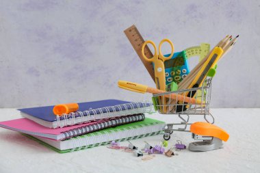 Gri arka planda kırtasiye malzemesi olan küçük bir alışveriş arabası.