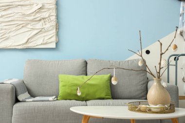 Şık bir oturma odasında, ağaç dalları ve Paskalya yumurtaları olan bir vazo.