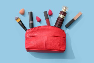 Kırmızı makyaj çantası, ruj, parfüm şişesi ve mavi arka planda makyaj malzemeleri.