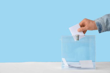 Mavi arkaplana karşı oy sandığının yanındaki oy veren adam.