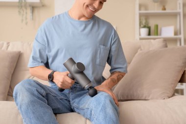 Genç adam evdeki koltukta bacağına perküsyon masajı yapıyor.