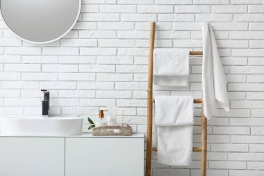 Banyodaki beyaz tuğla duvarın yanındaki merdiven üzerinde temiz yumuşak havlular.